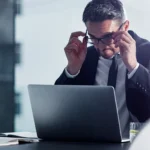 homem branco de terno sentado em frente ao computador sério lendo algo.