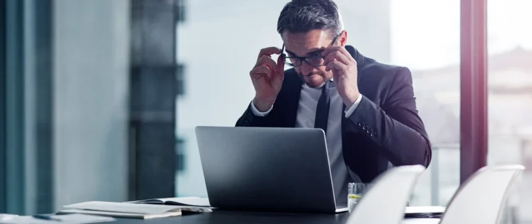 homem branco de terno sentado em frente ao computador sério lendo algo.
